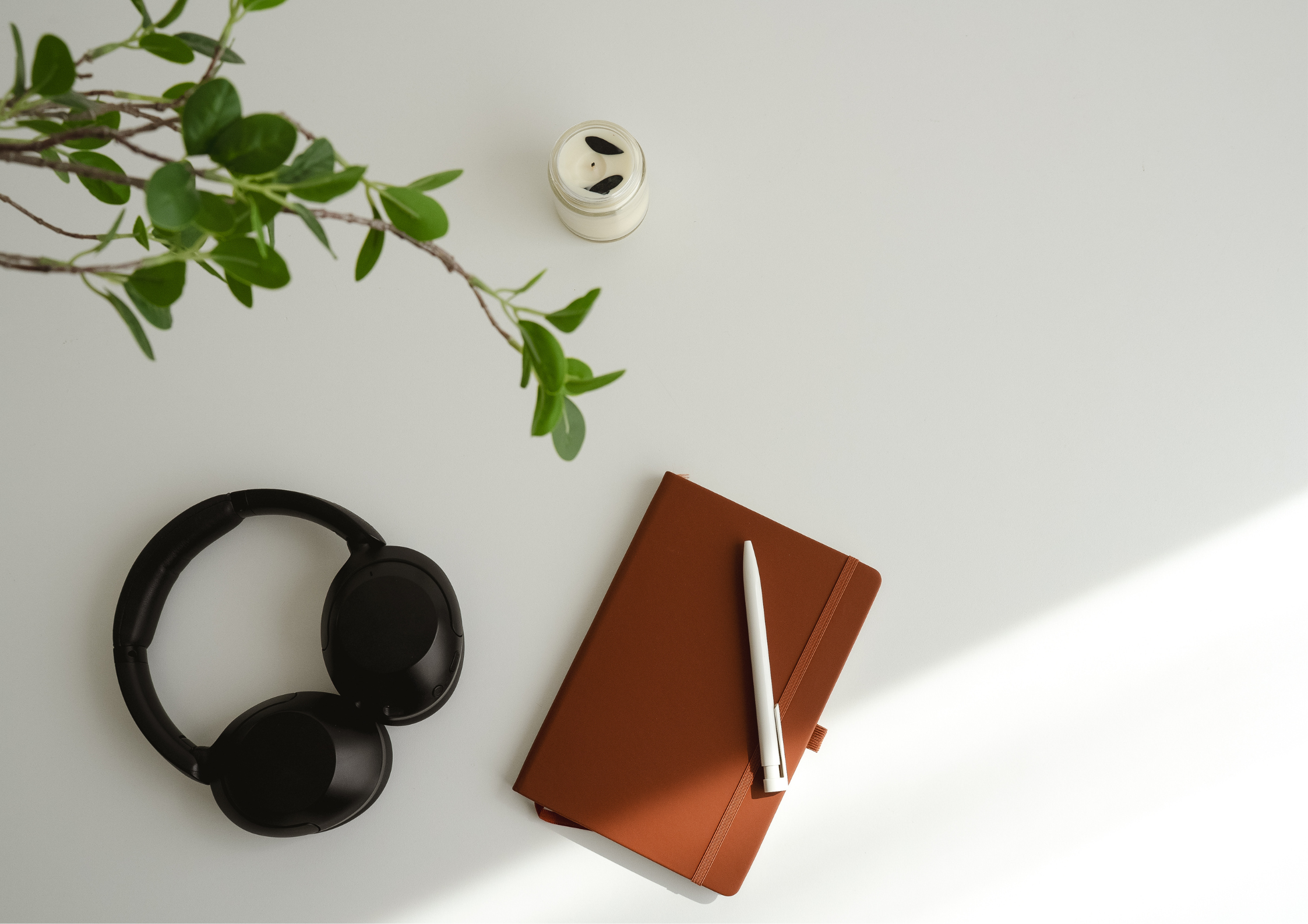 Minimalist flat lay with notebook, pen, headset, and small flower vase for a clean, modern aesthetic.