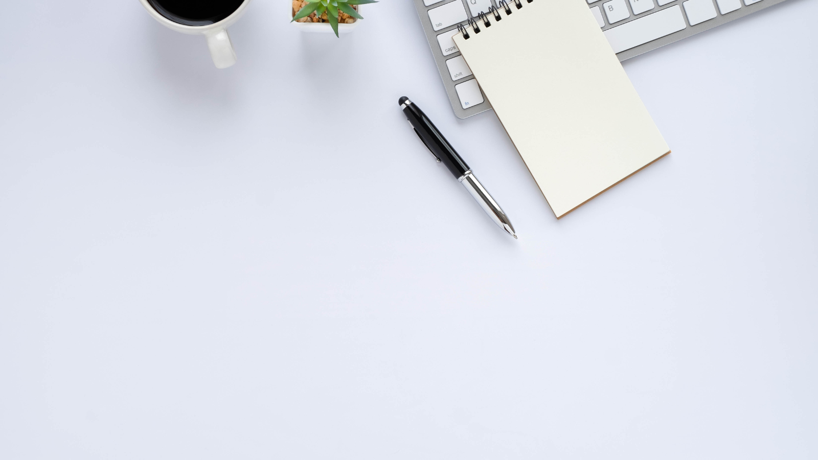 clean white background working table with a coffee, a ballpen, a pad and a laptop.