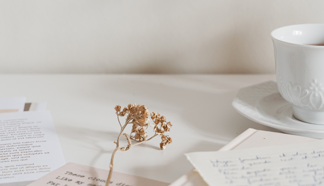 a cup of coffee and a dried flower with papers on top of the table